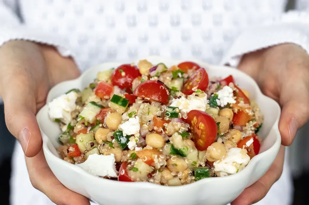 Feta-kikhernesalaattia valkoisessa kulhossa, jota pidellään kädessä.