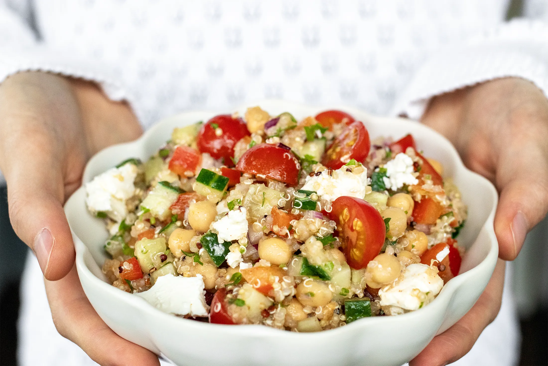 Feta-kikhernesalaattia valkoisessa kulhossa, jota pidellään kädessä.